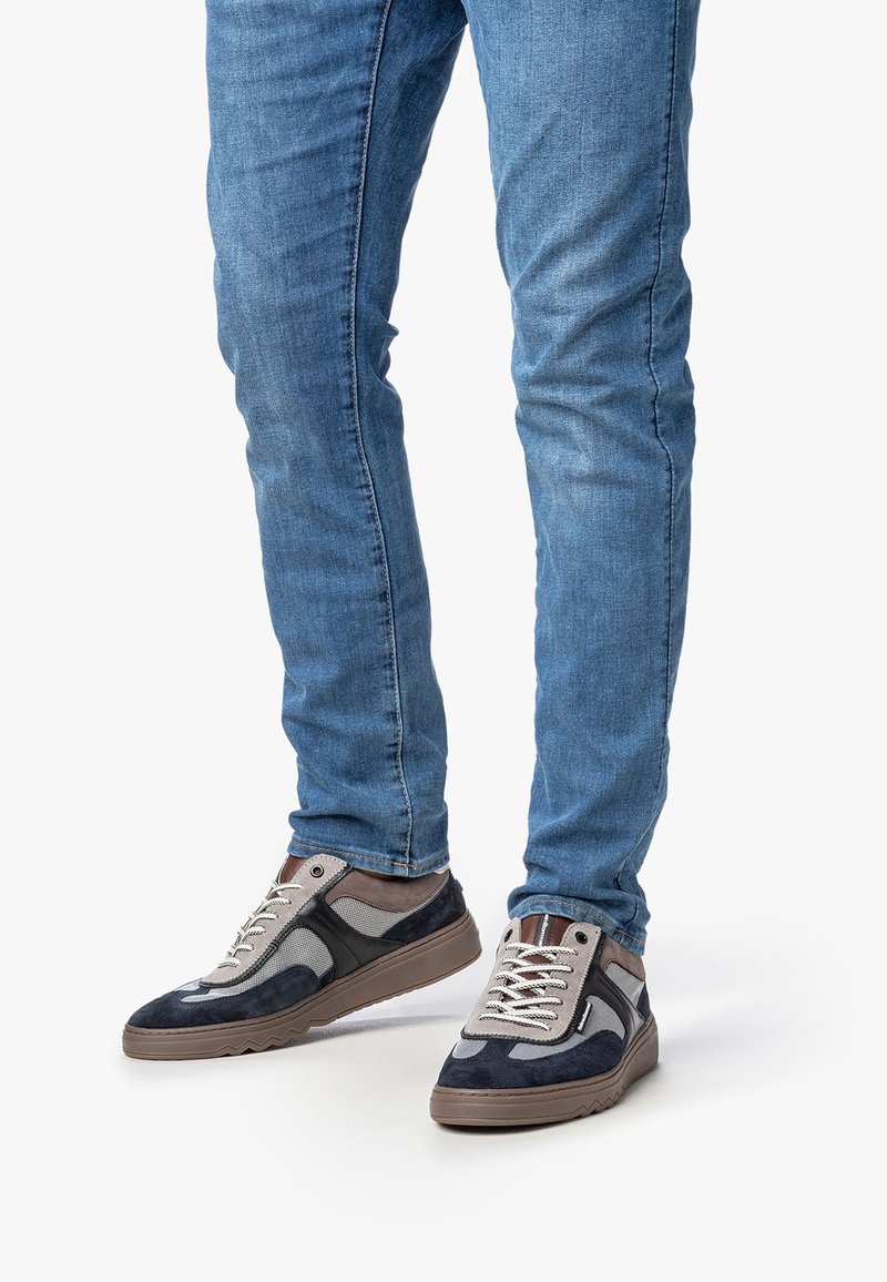 Sneaker aus einer Kombination von marineblauem Wildleder, grauem Stoff und braunen Akzenten. Gummisohle mit strukturierten Mustern, Schnürung vorne und weichem Innenraum.