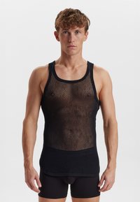 Schwarzes Mesh-Top mit Rundhalsausschnitt und ärmellosem Design. Verfügt über eine gemusterte Textur und eine taillierte Silhouette. Getragen über schwarzen Shorts.