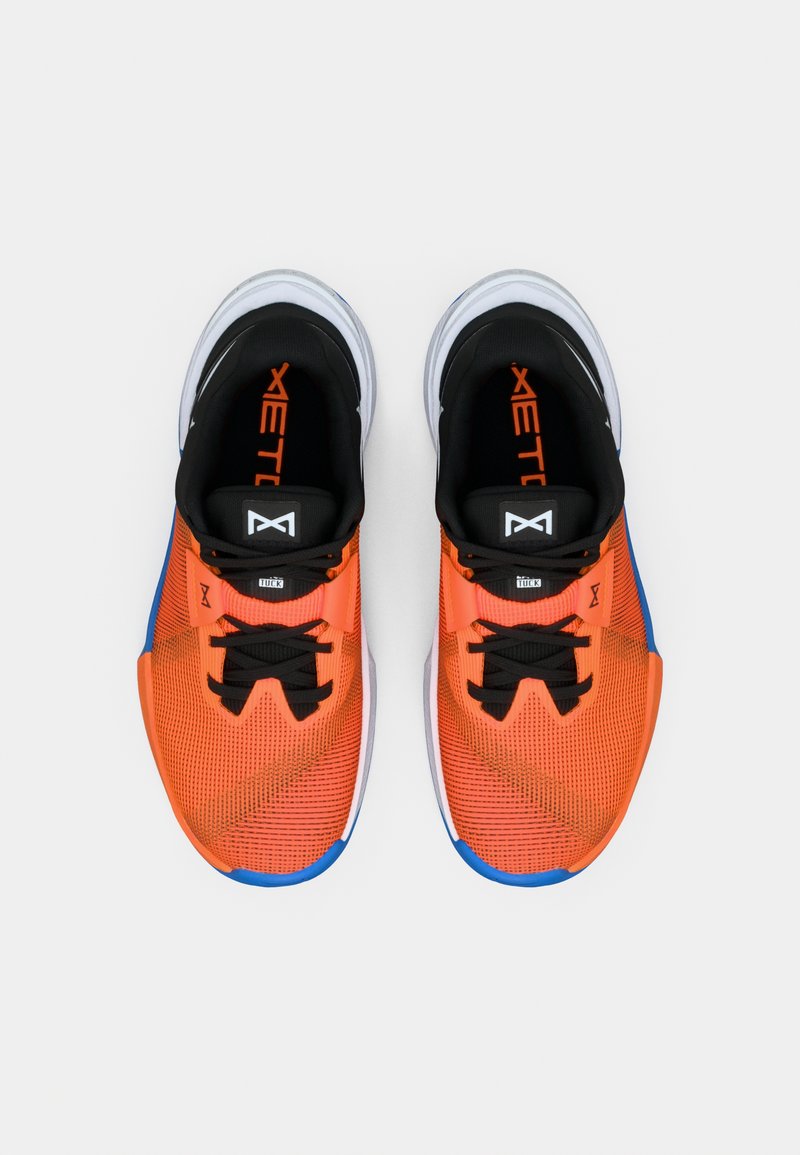 Un par de zapatillas deportivas de color naranja brillante y azul con cordones negros y suelas blancas acolchadas, vistas desde arriba sobre un fondo blanco.