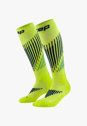Helle gelbe kniehohe Sportsocken mit vertikalen Streifenmustern in Dunkelblau und Hellblau sowie Polsterung um den Knöchel und Fuß.