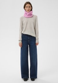 Világosszürke pulóver, bőszárú sötétkék farmer, és egy bordázott mintájú, rózsaszín kötött nyakmelegítő, apró márkajelzéssel.