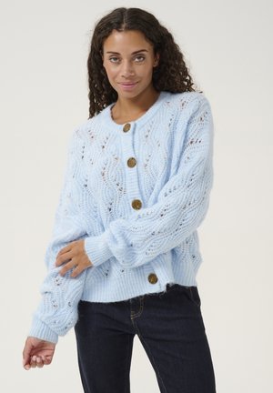 Cardigan en tricot bleu clair avec un design à motifs, encolure ronde et gros boutons marron. Tissu doux et texturé avec des poignets côtelés.