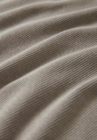 Texturerat tyg med smala, vertikala ribbor i mjuka beige toner, som visar milda vågor och veck för ökad djup och dimension.