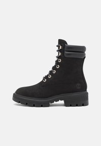 Bota de senderismo negra de ante con un collar acolchado, ojales metálicos y una suela de goma gruesa, diseñada para durabilidad y tracción.