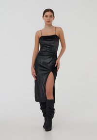 Abito midi nero con una texture scintillante, spalline sottili e uno spacco alto fino alla coscia. Indossato con stivali neri slouchy abbinati.