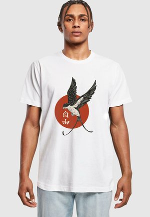 T-shirt en coton blanc présentant un graphique d'un oiseau aux ailes déployées au-dessus d'un cercle rouge, accentué de texte japonais en blanc.