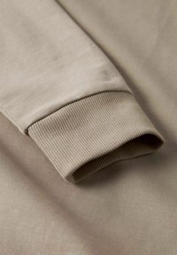 Närbild av en beige sweatshirtärm som visar ribbad mudd och slät bomullstextur.