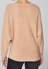 Beige grofgebreide trui met een losse pasvorm, driekwart mouwen en een ronde halslijn. Gestructureerde stof, aan de achterkant iets langer.