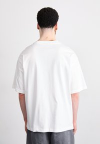 Camiseta blanca de manga corta con un corte holgado, escote redondo y material de algodón suave. Sin patrones ni gráficos visibles.