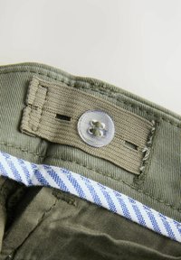 Tessuto verde oliva con chiusura a bottone sulla vita e un dettaglio interno a righe blu e bianche. Superficie texturizzata.
