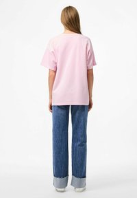 Maglietta di cotone rosa chiaro a maniche corte, abbinata a jeans in denim blu a vita alta con gamba ampia e orli sfilacciati.
