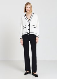Cardigan bianco con dettagli e bottoni neri, caratterizzato da un collo a V, tasche frontali, abbinato a pantaloni neri a gamba dritta e ballerine nere.