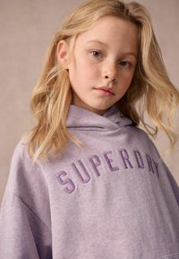Šviesiai violetinė gobtuvėlis su „SUPERDRY“ išsiuvinėtu tamsesnio atspalvio užrašu. Minkšta medžiaga, laisvas kirpimas ir didelis gobtuvas. Matoma subtili tekstūra.