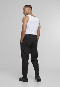 Svarte bukser med avslappet passform, med sidelommer og en glatt tekstur. Kombinert med en hvit tanktopp, sett bakfra.