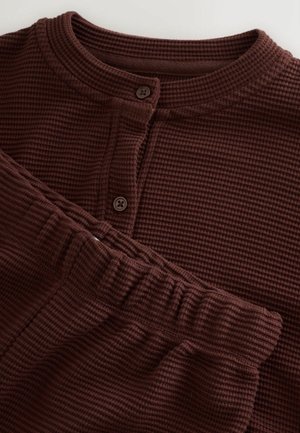 Barna, gofrás kötésű otthoni ruha szett, amely hosszú ujjú, gombos felsőből és elasztikus derékpántú, hozzáillő nadrágból áll.