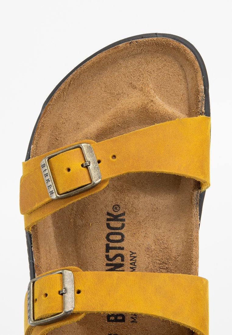 Sandale en cuir jaune avec deux sangles ajustables et boucles en argent. La semelle intérieure présente une texture de liège naturel et est estampillée du nom de la marque.