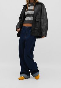 Veste oversize en cuir noir, crop top en tricot rayé gris et blanc, jeans bleu foncé amples et chaussures jaunes à enfiler avec des revers en denim.