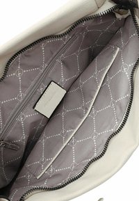 Weißes Lederhandtascheninnere mit grauem Futter, das ein Diamantmuster aufweist, einschließlich eines Reißverschlussfachs und eines zusätzlichen Einschubfachs.