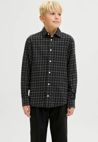 Melnā un balta šaha modeļa pogājamā krekla, kas izgatavots no mīkstas auduma, klasiskā apkakle un garas piedurknes, kopā ar brīviem melniem biksēm.