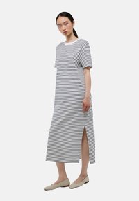 Robe maxi rayée en blanc et noir, avec des manches courtes, un col rond et une fente sur le côté. Tissu en coton lisse, design minimal.