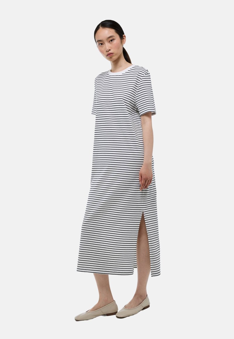 Robe maxi rayée en blanc et noir, avec des manches courtes, un col rond et une fente sur le côté. Tissu en coton lisse, design minimal.