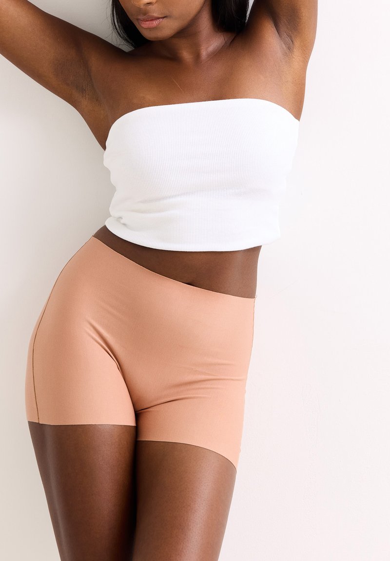 Lichtgewicht, geribd wit strapless topje en nude high-waisted shorts van gladde, rekbare stof. Naadloos ontwerp, minimale details.