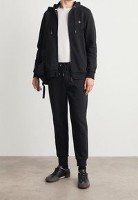 Svart zip-up hoodies med dragsko, i kombination med matchande svarta sweatpants och svarta sneakers. Outfiten har en enkel, minimalistisk design.