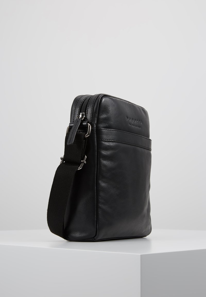 Czarna skórzana torba crossbody o gładkiej fakturze, z zamkiem błyskawicznym, regulowanym paskiem i wytłoczonym logo marki z przodu.