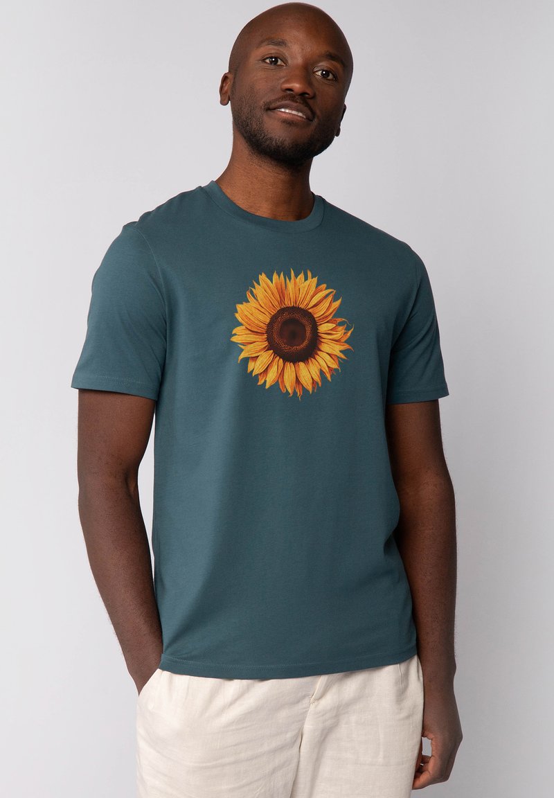 Türkises T-Shirt mit einem großen Sonnenblumenmotiv in der Mitte. Kurze Ärmel, runder Ausschnitt und weicher Baumwollstoff.