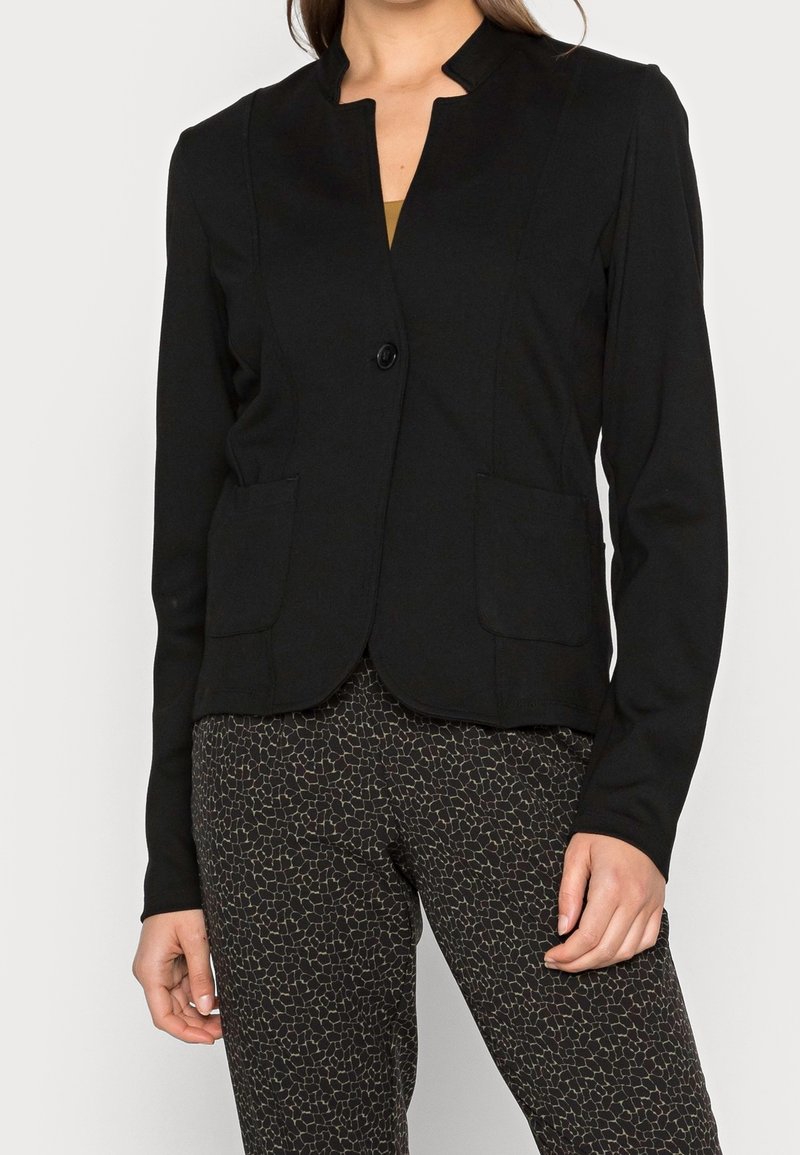 Blazer noir ajusté avec un col haut, fermeture à un bouton et deux poches avant. Matériau doux avec une texture lisse.