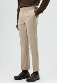 Beige op maat gemaakte broek met een slanke pasvorm, riemlussen, voorzakken, manchetten en een gladde textuur, gecombineerd met bruine loafers.