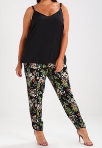 Haut sans manches noir avec de fines bretelles, associé à un pantalon à motif floral présentant de vives illustrations vertes, roses et blanches sur un fond noir.