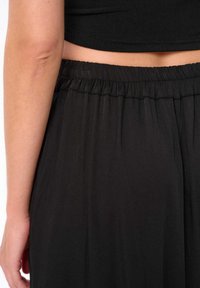 Zwarte rok met verzamelde elastische tailleband en vloeiend materiaal; gladde textuur met een subtiele glans; geen zichtbare patronen of hardware-details.