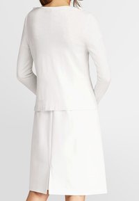 Bílý top s dlouhým rukávem a kulatým výstřihem, doplněný o odpovídající bílou sukni s rozparkem vzadu, vyrobený z měkké látky.