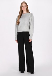 Jasnoszary, krótki sweter z bufkami i prążkowanymi mankietami, zestawiony z czarnymi, szerokimi spodniami. Gładka faktura, minimalistyczny design.