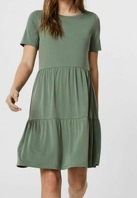 Kortsleeve klänning i knä längd av olivgrön tyg, med en utsvängd, lager på lager design och mjuk textur. Rund halsringning och avslappnad passform.