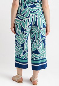 Hosen mit verkürztem Schnitt aus blauer Fabric mit einem großen grünen Blättermuster und weißen Akzenten. Elastischer Bund und detaillierte Säume am Ende.