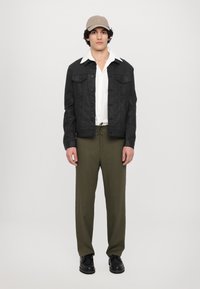Svart denimjakke med to brystlommer, hvit skjorte med krage, olivengrønne bukser og en beige caps. Svart snørebåndssko fullfører antrekket.