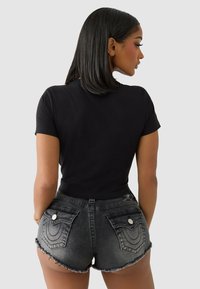 Black fitted t-shirt and high-waisted denim shorts. Shorts have frayed hems and decorative back pockets with a light wash and subtle stitching.