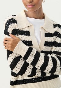 Pull en tricot avec col, présentant des motifs rayés alternés crème et noir. Design en crochet texturé avec des poignets côtelés.
