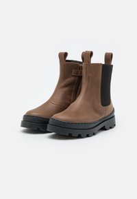 Bottes en cuir marron mi-hauteur avec une fermeture éclair sur le côté, un panneau élastique noir et une semelle en caoutchouc noir épaisse avec un motif de relief.