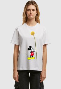 White cotton t-shirt featuring a graphic of Mickey Mouse in red shorts and yellow shoes, holding a yellow flower on a stick.