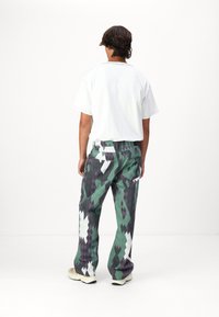 Un pantalon ample avec un motif en patchwork de diamants vert, noir et blanc. Associé à un t-shirt blanc uni et des baskets beiges.