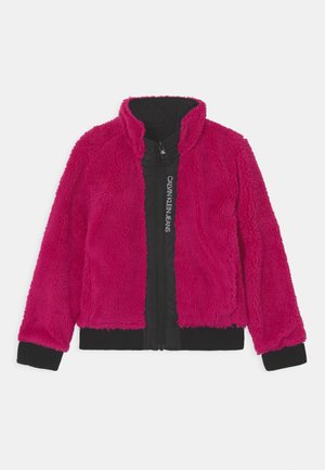 Chaqueta de forro polar rosa brillante con cremallera negra y forro en el cuello, con texto "Calvin Klein Jeans" en el panel frontal con cremallera.