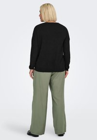 Black knit sweater with a relaxed fit, paired with light green wide-leg trousers. The sweater features a round neckline and long sleeves.