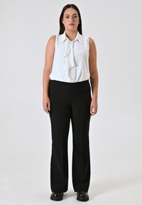 Witte mouwloze blouse met een gerimpelde voorkant, gecombineerd met hoge zwarte broeken en zwarte stevige schoenen. Eenvoudig en minimalistisch ontwerp.