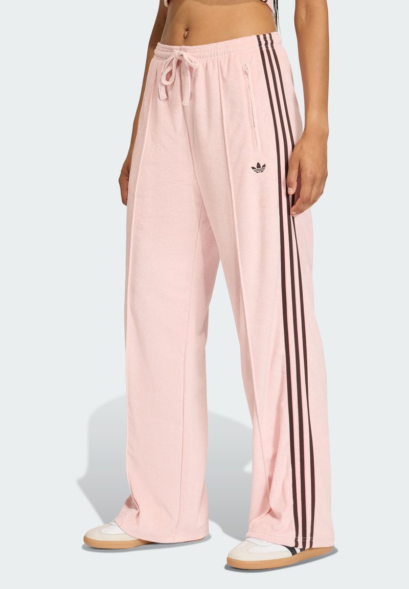 Pantaloni in felpa a gamba larga di colore rosa chiaro in tessuto testurizzato, con strisce laterali marroni e un logo ricamato sopra la tasca destra.