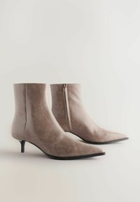 Bottines en cuir beige avec un bout pointu et un petit talon; présentent une fermeture à glissière latérale et une texture lisse et brillante.