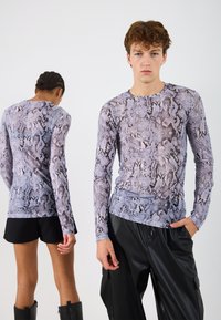 Top cu mânecă lungă într-un model cu imprimeu de șarpe purpuriu și negru, realizat dintr-un material neted și elastic. Asortat cu pantaloni scurți negri și pantaloni din piele.