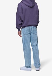 Fialová oversize mikina s jemnou texturou, spárovaná se světle modrými rovnými džíny. Obuv tvoří bílé tenisky s hladkým povrchem.